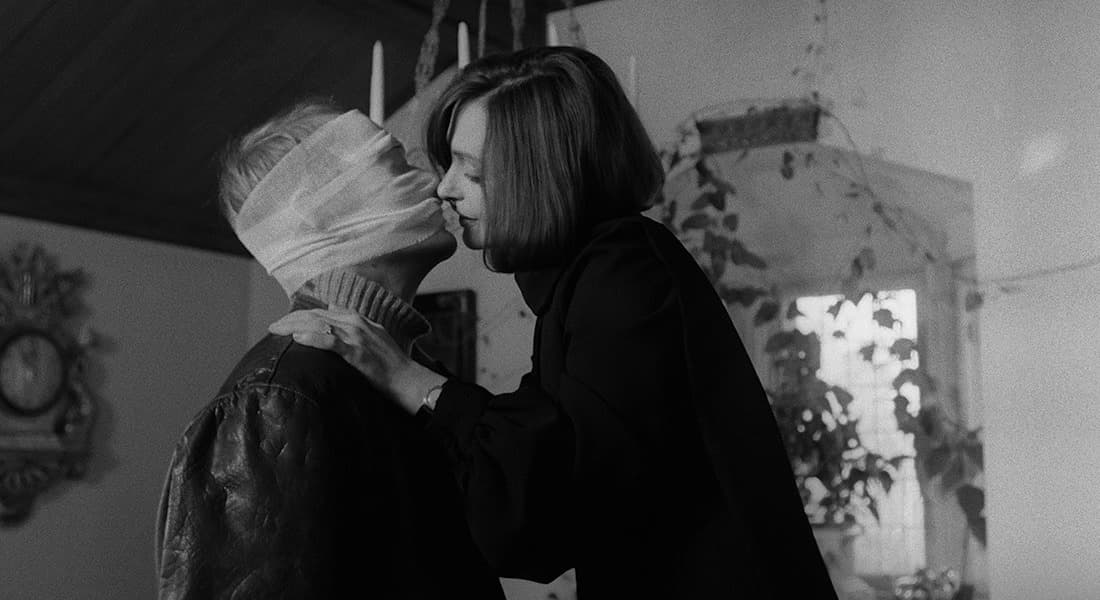 Bilde fra filmen 'Duett for kannibaler' av en kvinne i ferd med å kysse en mann med bandasjer rundt hodet.