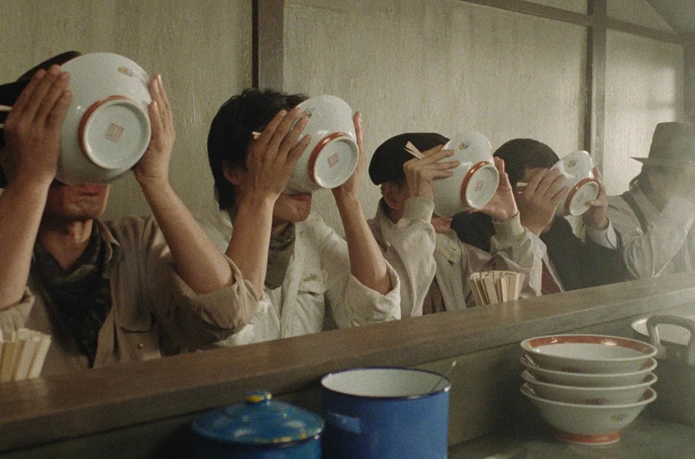 Bilde fra filmen 'Tampopo' av fire menn ved et bord som drikker fra ramen skåler.